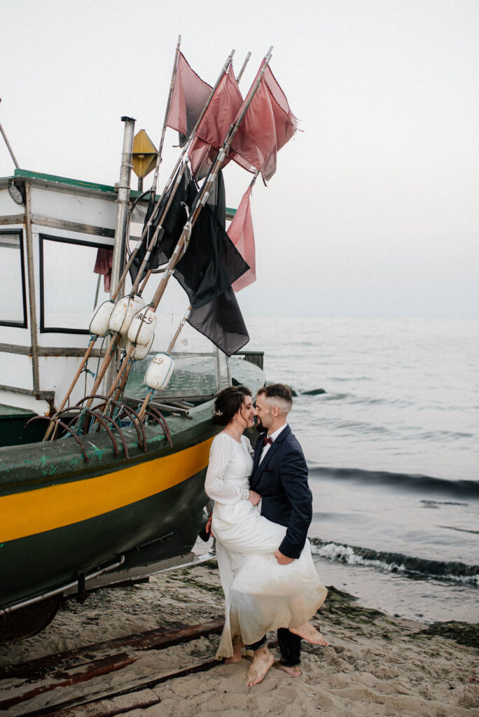 Pocałunek pary młodej opierającej sie o kuter rybacki nad morzem.